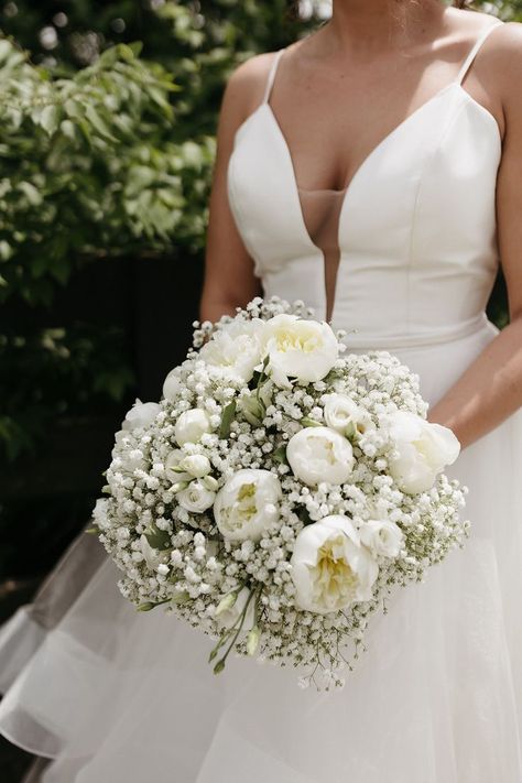 bride holding a round bouquet. The bouquet is all white and is made up of babys breath and peonies White Wedding Peonies, Simple Peonies Bouquet, Wedding Bouquets Bride Peonies, White Peonies Wedding Decoration, White Wedding Flowers Bridesmaids, Peony And Rose Wedding Bouquet, Wedding Bouquets Round, Peonies And Baby Breath Bouquet, Peony Roses Wedding Bouquet