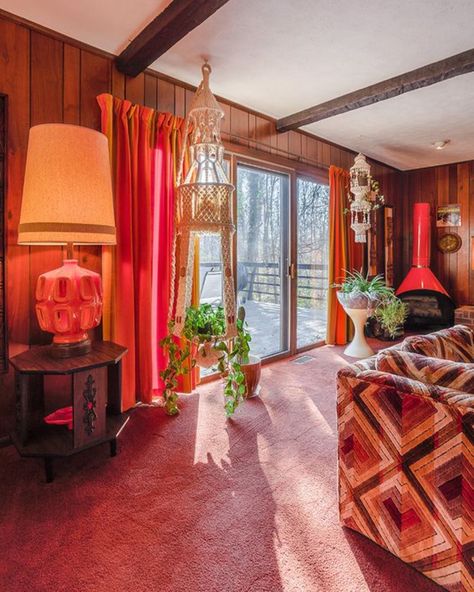 There is pink carpeting and dark wood paneling along all the walls. There is patterned couch partly in the frame on the right side, and in the back corner there is a red hearth. There are large sliding doors on the back wall that looks out to the back deck. There are two plant holders on either side of the sliding doors that are made of macrame. There is also a dark brown end table with a large red lamp on top. 70s Time Capsule Home, 1970 Apartment, 1970s Sunroom, 1970s Home Aesthetic, 70s Basement Aesthetic, 1970 Decor, 70s Basement, 70’s Living Room, 70’s Interior Design