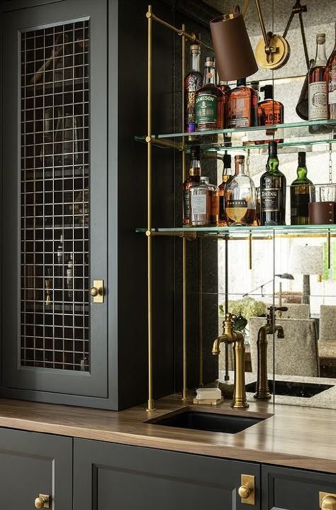 Beautifully appointed wet bar boasts glass and brass shelves fixed in front of a mirrored backsplash and over a small black sink with an antique brass faucet. Antique Mirror Backsplash Bar, Mirror Backsplash Bar, Antiqued Mirror Backsplash, Glass Bar Shelves, Modern Wet Bar, Antique Mirror Backsplash, Small Wet Bar, Mirrored Backsplash, White Brick Backsplash