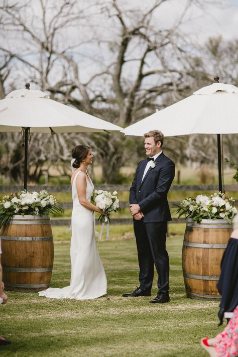 Wedding flowers by Scentiment Flowers, styling by Hire in Style, photo by Sarah Tonkin Photography, at Alverstoke Barn, south west Western Australia. Bride. Groom. Bridal bouquet. Boutonniere. Wedding ceremony. Ceremony flowers. Wine barrel flowers. Umbrella flowers. Green and white. Country wedding. Garden wedding. Farm wedding. Barn wedding. Summer wedding. Australian wedding. Historical property. Wedding Ceremony Wine Barrels, Wine Barrel Alter Wedding, Farm Wedding Australian, Wine Barrel Wedding Ceremony, Wine Barrel Flowers, Wine Farm Wedding, White Country Wedding, Flowers Umbrella, Umbrella Flowers