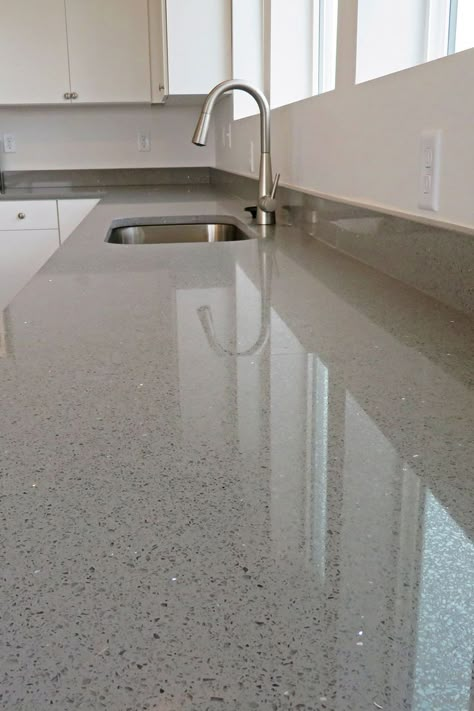 Close up of a countertop that is gray with black and silver flecks in it. Undermount sink with arched faucet and white cabinets with silver pulls are in the background Sparkly Quartz Countertops, Kitchen Sinks With White Countertops, White Countertops With Sparkle, White Glitter Countertops, Sparkling Countertops, Sparkly White Countertops, Non White Kitchen Countertops, Quartz Kitchen Countertops Sparkle White Cabinets, Modern Kitchen Cabinets White Grey Marble Countertops