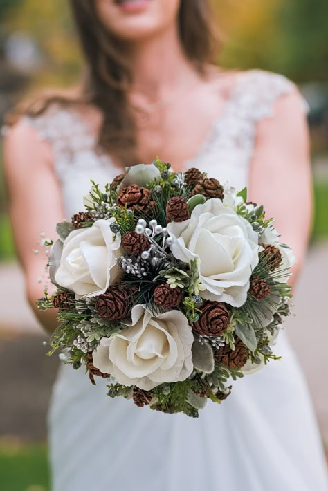 "For your winter wedding, this elegant bouquet of white Real Touch roses, pine, juniper, silver eucalyptus, silver berries and silver pine cones can be yours to have and to hold on your day in the spotlight.   We can work together to create a custom silk flower wedding package for your entire wedding party!  Contact us today and we can start planning! The bridal bouquet is shown at 10\" in diameter.  Select your custom ribbon color! You can select one of 5 sizes on this bouquet, with or without Winter Bridal Bouquets White, White Roses And Pine Cones, Wedding Bouquet With Pinecones, Pine Cone Bouquet, Woodsy Wedding Bouquet, Winter Bridesmaid Bouquet, Christmas Bridal Bouquet, Wedding Flowers Winter, Winter Western Wedding