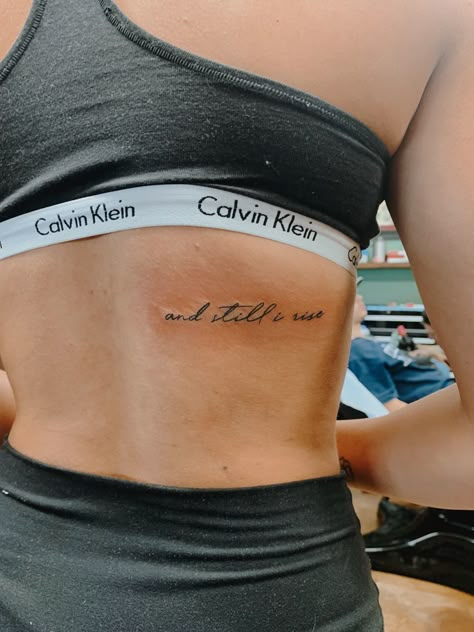 and still I rise tattoo Classy Word Tattoos For Women, Still She Rises Tattoo, Best Place For Word Tattoos, Strength Rib Tattoo, I Rise Tattoos For Women, Dainty Saying Tattoos, Hopeful Tattoos Ideas, Still I Rise Spine Tattoo, Women Word Tattoos