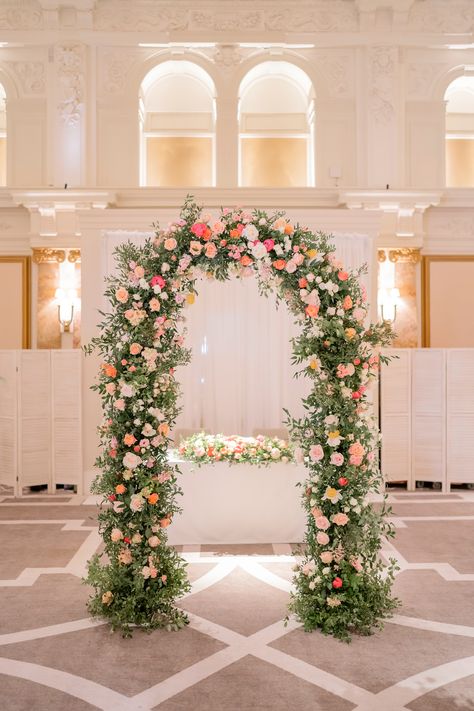 A foliage and floral ceremony altar arch with pink, peach and coral flowers. Wedding Beach Arch, Pink Floral Arch, Photographer Planner, Indian Food Menu, Wedding Foliage, Apricot Wedding, Coral Wedding Themes, Chuppah Decor, Wedding Walkway