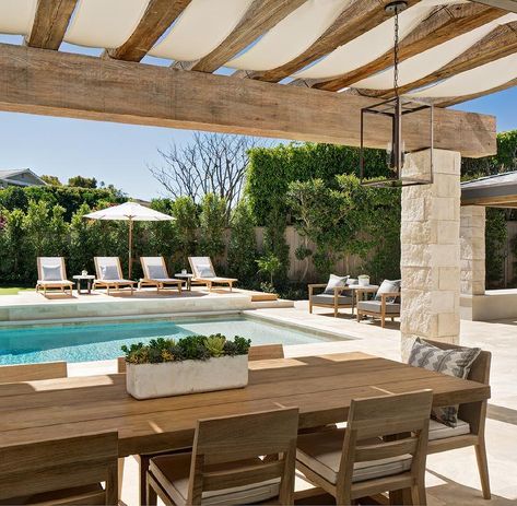 Stone pillars accent a rustic wood pergola finished with canvas and positioned over a teak plank dining table surrounded by teak slatted back dining chairs placed in front of an in ground swimming pool. Backyard Pergola, Casa Exterior, Backyard Inspo, Pergola Plans, Pergola Patio, Inspo Board, Pergola Designs, Dream Backyard, Outdoor Pergola