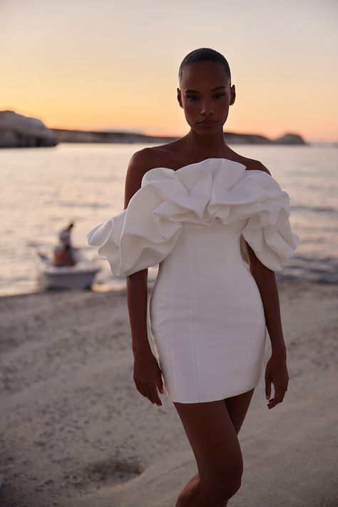 Stunning off-the-shoulder mini dress with a sleek, simple silhouette, embellished with oversized ruffled sleeves made of soft yet structured fabric. The clean lines of the fitted bodice and skirt give this outfit a modern aesthetic. Structured Mini Dress, Eva Lendel, Structured Fabric, Bridal Elegance, Venus Dresses, 2025 Wedding, Simple Silhouette, Sheer Material, Ruffled Sleeves