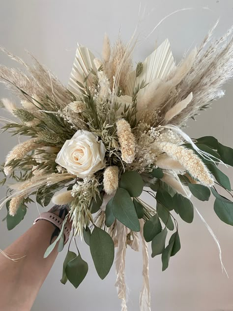 Celebrate your special day with the timeless beauty of this dried flower wedding bouquet! The bouquet is composed of delicate cream colored roses and florals that are carefully arranged to create an eye-catching presentation. Crafted with great attention to detail, this bridal flower arrangement is perfect for those looking for a unique and charming alternative to fresh flowers. The dried flowers retain their natural beauty and texture while providing a long-lasting keepsake from your wedding da Dried Palm Bridesmaid Bouquet, Sage Green Dried Flower Arrangements, Dried Flower Bridal Bouquet Eucalyptus, Dried Flower Hoop Wedding, Green And White Bridal Bouquet Dried Flowers, Dried Flower Bouquet Green, Pampas And Eucalyptus Bouquet, Rose Pampas Bouquet, Pampas And Eucalyptus Wedding