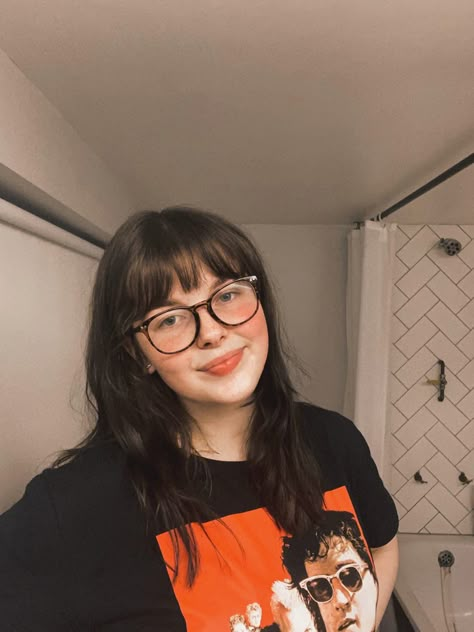 Brunette haired girl with bottleneck bangs and round tortoise shell glasses smiling in a Lost Boys graphic t-shirt. Background is a white bathroom. Haircuts Fringe Bangs, Glasses With Bangs Fringes, Glasses Bangs Hair, Choppy Bangs Round Face, Bangs For Round Face Plus Size, Fringe Bangs On Round Face, Round Glasses With Bangs, Short Bangs Glasses, Whispy Front Bangs With Glasses