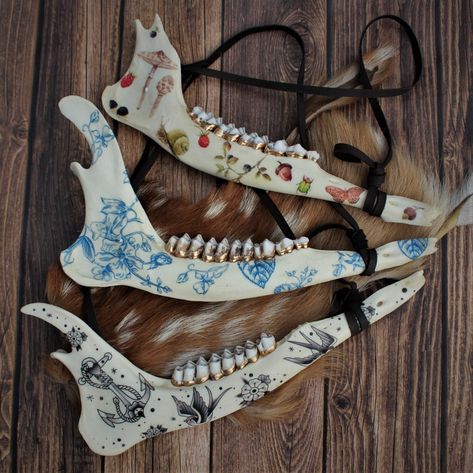 Deer Jawbone | Wall hanging decor real bone painted skull deer animal teeth gold vulture culture delft cottage core tattoo oddities tooth Each of these deer jawbones have been adorned with a variety of vintage-style illustrations, perfect for any naturalist or entomology lover. Jawbones are from whitetail deer, naturally found and nature-cleaned, then gently sanitized and whitened. The back has an attached triangle hanger as well as a deerskin leather lace, ready for wall installation. These pie Animal Bone Projects, Painted Deer Jaw Bone, Bone Hanging Decor, Cow Jaw Bone Art, Painted Bones Art, Animal Jaw Bone Art, Painted Jaw Bone, Deer Bone Art, Animal Bone Crafts