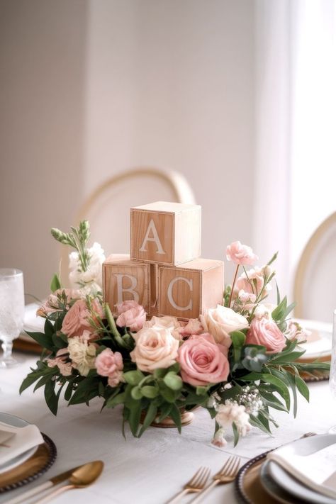 A Baby Shower centerpiece featuring wooden blocks labeled "A," "B," and "C" crowns a floral arrangement of pink and white roses with greenery. This charming display adorns a dining table set with white tableware and gold cutlery, all under soft lighting. Vintage Baby Shower Theme, Storybook Baby Shower Theme, Unique Centerpiece Ideas, Baby Shower Centerpiece Ideas, Retro Baby Showers, Baby Blocks Baby Shower, Gender Reveal Baby Shower Themes, Whimsical Baby Shower, Unique Baby Shower Themes