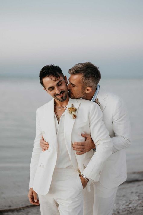 Groom in mens white wedding suit with dusky orange garden rose and dried flower boutonniere, white shirt and silver jewellery standing on the beach with Groom wearing white blazer, light blue and white striped shirt and dusky orange garden rose and dried flower boutonniere | LuxArt Wedding Studio Mens White Wedding Suit, White Suit Groom & Groomsmen Suits, White Summer Wedding Suit, Elopement White Suit, Unstitched White Wedding Suit, Gay Beach Wedding, White Wedding Suits For Men, Groom And Groomsmen Outfits, White Wedding Suit