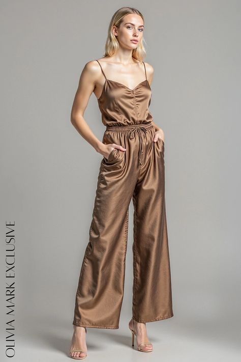 Its satin fabric, in a warm, earthy bronze, drapes gracefully, promising comfort while exuding luxury. The wide-leg cut flatters with a fluid motion, while the elastic waist with a delicate drawstring offers a customizable fit. A plunging neckline adds a touch of allure, making this jumpsuit a versatile piece for any occasion, from a chic day out to a glamorous evening event. Uzun Boy, Light Palette, Jumpsuit Elegant, Olivia Mark, Plunging Neckline, Tulum, Satin Fabric, Drawstring Waist, Leg Pants