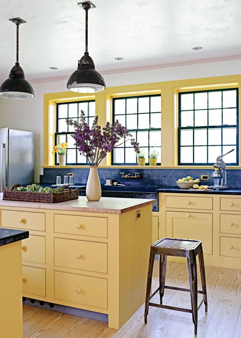 A golden-yellow island gives this kitchen a peppy focal point. The island paint color matches the surrounding cabinets and trim, but a contrasting butcher-block countertop helps the prep space stand out. Black accents and dark soapstone surfaces introduce a modern edge to the soft yellow kitchen. #kitchen #kitchenideas #kitchenislandcolors #kitchenremodel #bhg Kitchen Color Combos, Popular Kitchen Colors, Yellow Kitchen Designs, Kitchen Color Trends, Kitchen Colour Combination, Interior Window Trim, Yellow Cabinets, Bold Kitchen, Painted Cabinets