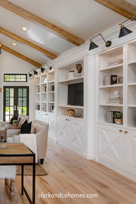 White oak flooring and ceiling beams, with white built-ins and accented by black light fixtures all contribute to the look of this Modern Farmhouse great room. #greatroom #modernfarmhouse #woodflooring #ceilingbeams #builtins #shiplapceiling Built Ins With Ceiling Beams, Built In With Lights, Floor To Ceiling Entertainment Center, Floor To Ceiling Built Ins, Modern Farmhouse Built Ins Living Rooms, Built Ins With Sconces, Greatroom Builtins, Modern Farmhouse Built Ins, Floor To Ceiling Cabinets Living Room