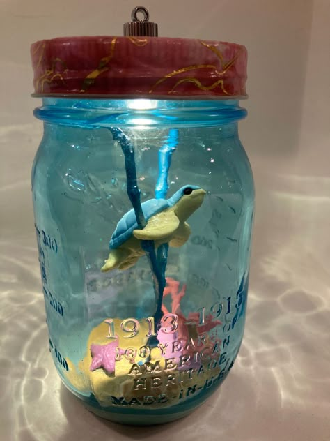 Mason Jar Night Light "Bottle Scape" with a whimsical underwater scene. A sea turtle is swimming above the sandy ocean bottom. Pink corals, a sea star and a shell are visible on the ground. The glass has a beautiful turquoise tint, which gives the appearance of an aquarium filled with water. The ocean themed mason jar can be illuminated with an LED light in the lid, and gives off a soft light.  Please note that this decoration is not suitable for children under 3 years because the light contains Mason Jar Aquarium, Bri Cheese, Ocean Themed Crafts, Glass Jar Crafts, Things To Do With Jars, Turtle Bedroom, Ocean In A Bottle, Turtle Room, Mason Jar Night Light