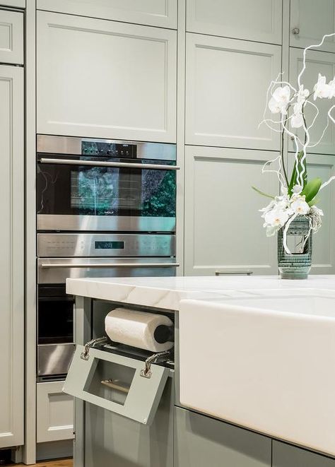 Fitted with a farmhouse sink and a built-in drop down paper towel holder, a gray kitchen island is topped with a marble countertop and positioned beside stacked gray floor-to-ceiling cabinets beautifully framing a stainless steel microwave fixed above a stainless steel oven. Paper Towel Storage, Kitchen Island Tops, Floor To Ceiling Cabinets, Grey Kitchen Island, Kitchen Transitional, Kitchen Paper Towel, New House - Kitchen, Kitchen Island Design, Grey Flooring