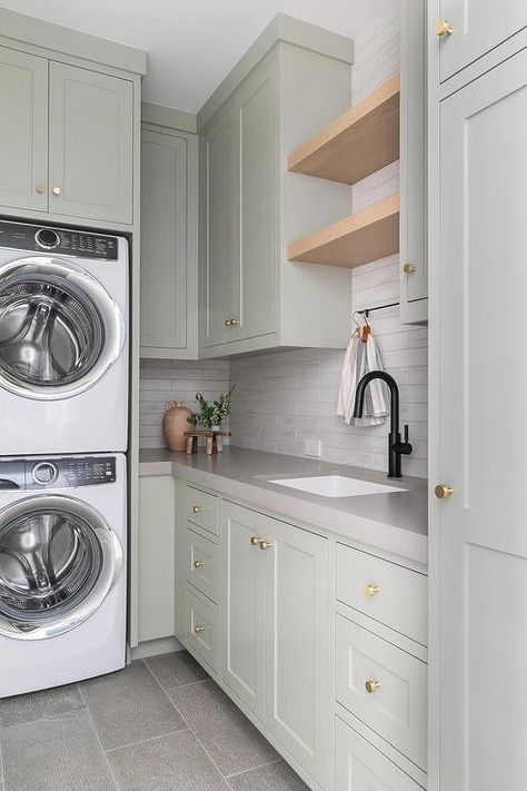 A stacked white front loading washer and dryer are enclosed beneath light gray green cabinets. Transitional Laundry Room, Grey Laundry Rooms, Laundry Room Colors, Stacked Laundry Room, White Laundry Rooms, Green Laundry, Dream Laundry Room, White Laundry, Laundry Cabinets