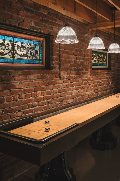 Shuffleboard! A basement converted into a 1920's speakeasy-style man cave. Design features include reclaimed brick, antique stained glass windows, scalloped pendant lighting and concrete flooring. Designed by Fabian Genovesi and built by Neil Kelly Company in Portland, Oregon. Adu Decor, Basement Speakeasy, Bar Lounge Room, Speakeasy Decor, 1920s Speakeasy, Daylight Basement, Whiskey Room, Cave Basement, Speakeasy Bar