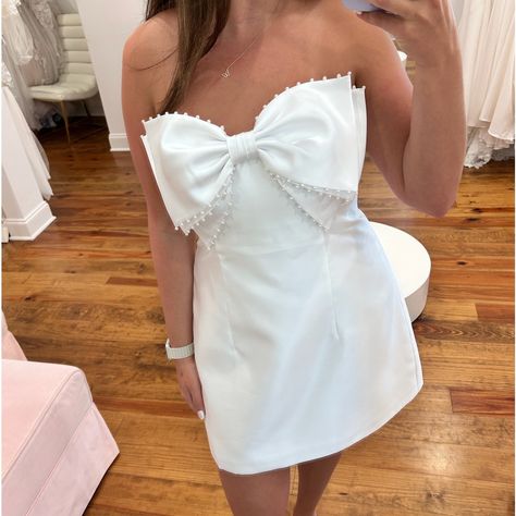 This Super Cute Little White Dress Epitomizes Sleek-Meets-Chic With A Playful Twist. Front And Center Is A Handcrafted Oversized Bow Dotted With Pearls For A Subtle Bling Factor. The White Luxe Satin Twill Fabric Glows With A Subtle Sophistication, Serving Up A Totally Stunning Strapless Mini Dress. Cocktail, Princess Waist, Bow, Buttons. 100% Poly Imported Sweetheart, Strapless, Satin Twill. Mini Dress Cocktail, Black Bow Dress, Alfred Sung, White Strapless Dress, Little White Dress, Pearl Dress, White Short Dress, Dress Cocktail, Reception Dress