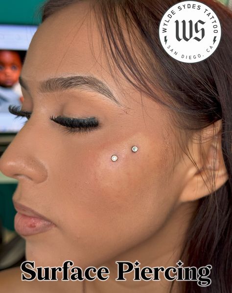 Surface piercings are different from dermal implants - they are a single piercing using a surface bar. All jewelry used is hypoallergenic implant-grade titanium for sensitive skin. For piercing prices, check out our website at www.wyldesydestattoo.com or call 619-575-6792 #bodypiercing #piercing #surfacepiercing #wyldesydestattoo #sandiego #piercingstudio Surface Cheek Piercing, Chin Piercing Women, Surface Piercing Face, Dermal Face Piercing, Dermal Piercing Face, Face Dermal Piercing, Anti Eyebrow Piercing, Chin Piercing, Face Dermal