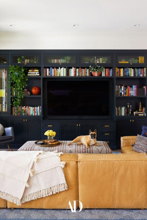 Inspired by an awakening of wanting a home that represented who they truly are, color was quickly allowed to reign supreme in the home of actors Daveed Diggs and Emmy Raver-Lampman. In the living room, the couple’s French bulldog, chills on the family room’s custom-made ottoman. #livingroom #livingroominspo #livingroomideas #familyroom #sofa #couch #leather #ottoman #entertainmentcenter #puppy #rug #curtains #sectional #books #floorlamp Media Area Living Room, Architectural Digest Family Room, Unique Family Room Ideas, Colorful Ottoman Living Room, Readers Living Room, Best Family Rooms, Playful Family Room, Family Room Leather Sectional, Living Room Setup With Tv