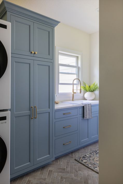 This beautiful blue laundry room is the perfect color for spring and summer. There is a stacked washer and dryer along with a gold sink and a small house plant on the window. Gold hardware + blue laundry room + laundry room design + interior design + bodine white + summer interior design + spring interior design + summer color palette + blue color palette + blue paint + laundry room inspo Blue Cabinet Laundry Room, Blue Cabinets Laundry Room, Baby Blue Laundry Room, Blue Laundry Room Cabinets, Mudroom Laundry Room Ideas, Laundry Room Decorating, Blue Laundry Rooms, Mudroom Cabinets, Mudroom Organization