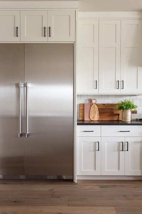 A stainless steel double door refrigerator is recessed beneath white shaker cabinets finished with oil rubbed bronze hardware. Stainless Fridge, Steel Double Doors, Large Fridge Freezer, White Shaker Kitchen Cabinets, Stained Kitchen Cabinets, Kitchen Styling Modern, Oil Rubbed Bronze Hardware, Stainless Steel Kitchen Appliances, White Shaker Kitchen