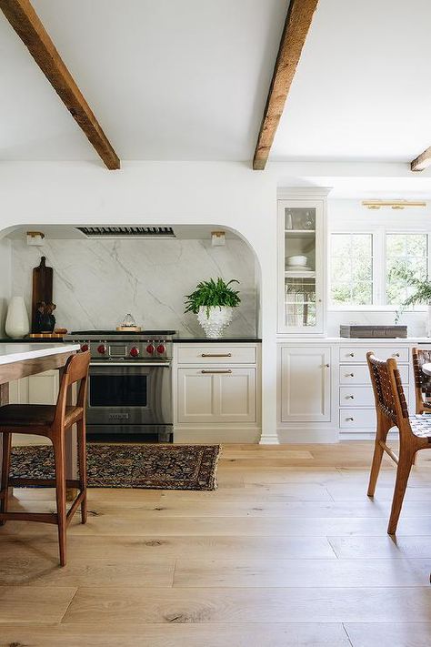 A curved stone cooking alcove is fitted with a Wolf range placed between light gray kitchen cabinets adorned with aged brass hardware and contrasted with a black countertop. Stove Alcove, Kitchen Trends 2021, Alcove Ideas, Jean Stoffer Design, Tudor Kitchen, Jean Stoffer, Top Kitchen Trends, Family Room Remodel, Style Me Pretty Living