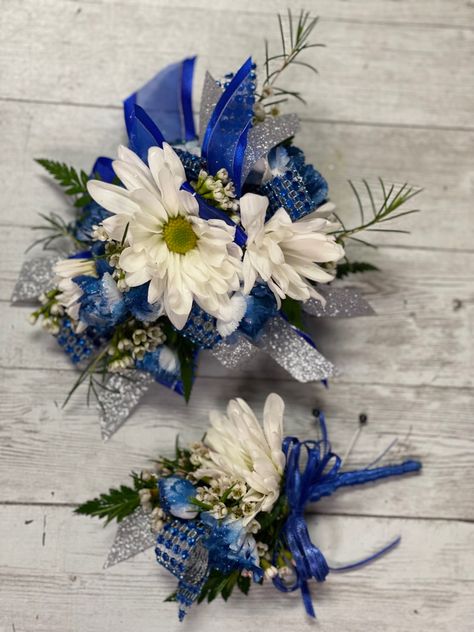 White daisies, tinted royal blue mini carnations with royal blue glitter sprinkled on them.  We used wax flower for fill and royal blue and silver ribbon. Royal Blue Homecoming Flowers, Royal Blue And Silver Corsage, Royal Blue Corsage And Boutonniere Prom, Royal Blue And White Corsage, Blue And Silver Corsage, Royal Blue Corsage And Boutonniere, Blue And White Corsage, Royal Blue Corsage, Hoco Corsage