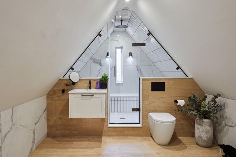 In a loft guest ensuite transformation, we optimized space by replacing the bath with a spacious shower featuring wrap-around seating. The design elegantly contrasts white metro tiles with a high-pitched loft ceiling. A low-level wall accommodates the basin unit and WC, while gunmetal brassware and black finishes add sophistication. The bespoke shower area frames a narrow window, adding a touch of grandeur. Low Ceiling Loft Conversion, Shower Under Eaves, Shower With Angled Ceiling, Small Attic Ideas Low Ceilings, Small Attic Ideas, White Metro Tiles, Loft Ensuite, Guest Ensuite, Narrow Window