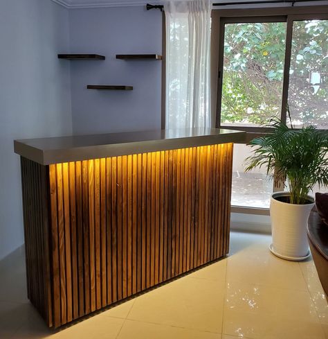 Made a wooden bar counter for a client in Bahrain. The stained wood slats were randomly placed to create an effect on the fascia of the counter. The brass color counter top was given a slight glossy effect, whereas the body of the counter was in matt. Added LED strip lights to enhance the beauty of the bar. Also added wooden stained shelves. Standing Bar Counter, Slat Wall Led Strip, Wooden Bar Shelves, Restaurant Billing Counter Design, Bar Reception Design, Wooden Counter Design, Wooden Bar Ideas, Black And Wood Bar, Wood Bar Design