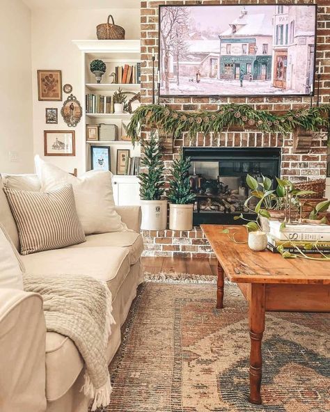 A Pine garland is hung across a red brick fireplace in this living room. Two miniature pine trees in white planters are set on the hearth below, next to a white shelf filled with books. A wood coffee table is decorated with a trailing plant and a votive candle on top of a stack of books...   Image: lakefrontfarmhouse Red Brick Fireplace, Shiplap Living Room, Farmhouse Fireplace Ideas, White Stone Fireplaces, Red Brick Fireplaces, White Brick Fireplace, White Mantel, Wood Coffee Table Rustic, White Shiplap Wall