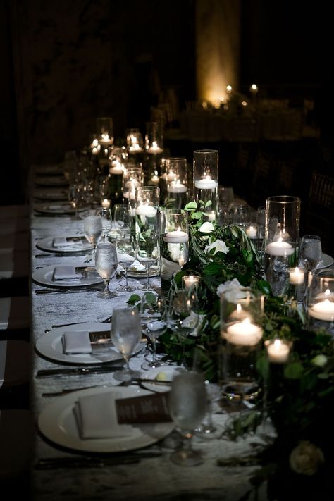 A modern long hed table decorated with silver linen, lush greenery with pops of white flowers, and a mix of varying size floating candles and votives. Philadelphia Ritz Carlton Wedding. PC Alison Conklin Photography https://www.alisonconklin.com/ Floating Candles And Greenery, Greenery Candles Wedding, Candle Greenery Centerpiece, Candles Reception, Greenery Wedding Theme, Ritz Carlton Wedding, Floating Candles Wedding, Long Table Wedding, Cylinder Candles