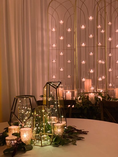 Firefly Ambiance createtd these gorgeous centerpieces with geometric vesselss fill of twinkle lights. The effectt was stunning and created a dreamy, romanic ambiance for this wedding reception. Gold candles and greenery were added to the cenetrpieces and a custom candle screen backdrop was created to transform the space. #receptionideass #receptiondecor #weddingideass #twinklelights #fireflyambiance #geometricdecor #geometricwedding #eventlighing #backdrop #candledecor #eventbackdrop Fairy Lights Wedding Centerpieces Vases, Twinkle Lights Wedding Table Decor, Twinkle Lights Wedding Centerpiece, Candles And Twinkle Lights Wedding, Twinkle Lights Centerpiece, Firefly Centerpiece, Twinkle Light Centerpiece Wedding Ideas, Twinkle Lights Wedding Decor, Fairy Light Centerpiece Wedding