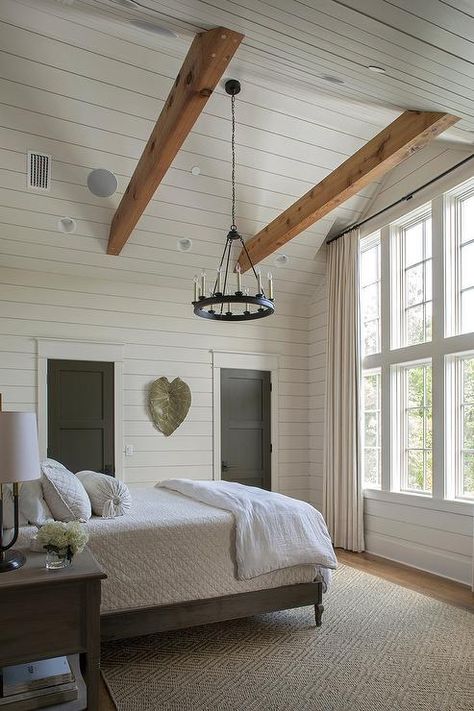 Cottage bedroom with gray shiplap vaulted ceiling features two oak wood beams and a small candelabra chandelier over a gray wood bed. Beams In Vaulted Ceiling Bedroom, Vaulted Ceiling With Cross Beams, Farmhouse Vaulted Ceiling Bedroom, Vaulted Ceiling Small Bedroom, Lighting For Vaulted Ceilings Bedroom, Half Vaulted Ceiling With Beams, Exposed Beams Ceiling Bedroom, Small Bedroom Vaulted Ceiling, Cathedral Bedroom Ceiling