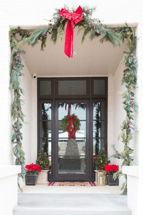 Our white brick exterior with fresh Christmas garland and red bows. Christmas wreath with gold bells and a red bow. Silk poinsettias in a copper pot on the front porch, black glass front door. Black Glass Front Door, Fresh Christmas Garland, White Brick Exterior, Exterior Christmas Decorations, Porch Garland, Christmas Wreaths For Windows, Christmas Pfps, Affordable Christmas Decorations, Ideas Christmas Tree