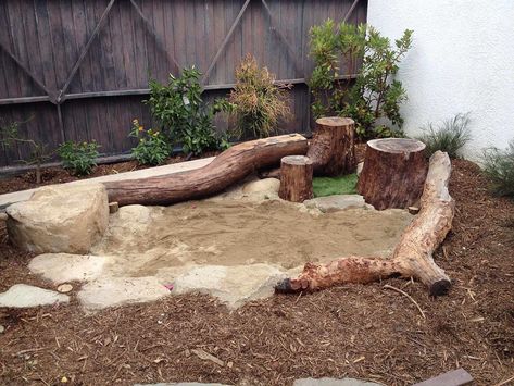 Rustic backyard play area with a sandbox that is surrounded by tree trunks and wooden logs | How to Create a Kid-Friendly Backyard that Even Adults Can Enjoy | Decoist Log Play Area, Unique Sandbox Ideas, Log Sandpit, Natural Sandbox Ideas, Natural Playscapes Backyard, Diy Nature Play Backyard, Easy Diy Sandbox Ideas, Natural Play Areas For Kids, Rock Pit Play Area