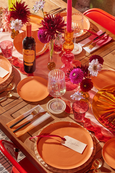 1. A table runner in shades of pink and red create the base of the tablescape. The clashing shades and tones will give the overall tablescape a playful mis-matched vibe.

2. Place a variety of candlesticks and small, multi-coloured vases of flowers dotted down the runner. 

3. Layer terracotta orange shaded plates over woven rattan placemats for an organic feel. Brassy cutlery and dip-dyed napkins bring additional pops of warmth and texture. Colourful Wedding Tablescape, Pink Orange Yellow Tablescape, Sunset Table Decor, Pink Orange Table Setting, Pink And Orange Dinner Party, Pink And Orange Tablescape, Pink And Orange Table Setting, Orange Tablescape, Hosting Aesthetic