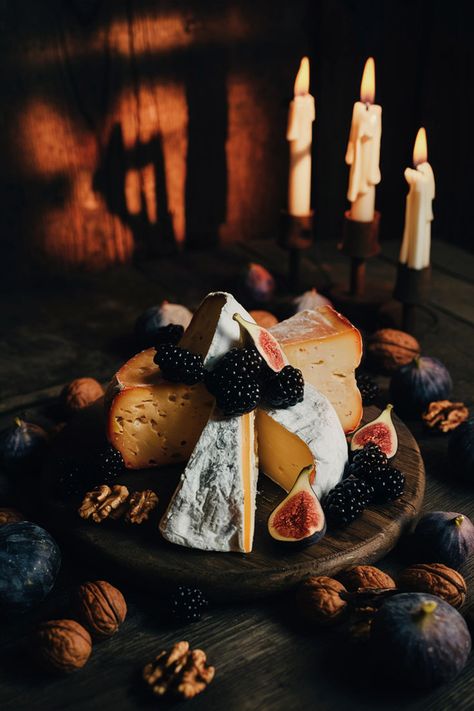 A rustic cheese board with dark wood, featuring aged cheeses, blackberries, figs, and walnuts, illuminated by candlelight with a gothic, moody ambiance. Dark Aesthetic Food Photography, Samhain Charcuterie Board, Vintage Charcuterie Board, Dark Charcuterie Board, Halloween Food Photography, Halloween Speakeasy, Academia Food, Cheese Board Aesthetic, Dark Academia Food