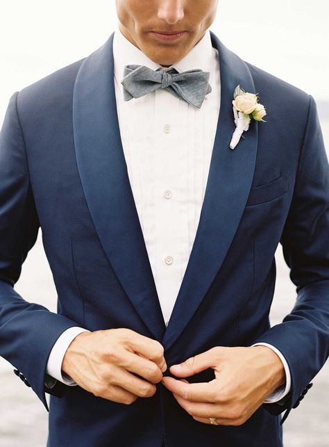 groom-buttoning-up-navy-blue-tuxedo-jacket-with-grey-bow-tie-white-shirt-ivory-flower-boutonniere Blue Suit Bow Tie, Wedding Suits Men Blue, Wedding Suits Men Grey, Navy Groom, Navy Suit Wedding, Lake House Wedding, Grey Suit Wedding, Wedding Tux, Blue Suit Wedding