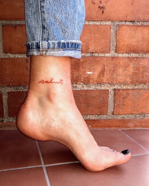 Tattoo word in red ink on ankle Ankle Tattoo With Words, Ankle Tattoo Small Words, Word Tattoo On Ankle, Name Tattoo On Ankle, Ankle Lettering Tattoo, Outside Of Ankle Tattoo, Above The Ankle Tattoo, Back Of Ankle Tattoo Words, Ankle Tattoos For Women Words