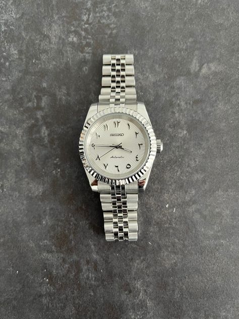 This watch is based on the Datejust with Arabic numerals. Rolex was one of the first luxury watch brands to produce watches with Arabic numerals back in the 1950s. They continued producing these for the Middle Eastern markets until the late 1970s. It wasn't until 2016 that Rolex reintroduced the dials with Arabic numerals. First for the Day Date, which was shortly after followed by the Datejust and the Daytona. In recent years the dials with Arabic numerals have become quite popular. Various brands (e.g., Breitling, Patek Philippe, Audemars Piguet, Jaeger LeCoultre, IWC) have started producing dials with Arabic numerals. Watches with Arabic numerals have been featured on the wrists of Cristiano Ronaldo, Jay-Z, Drake, DJ Khaled, Tom Brady and Mark Wahlberg.The white/silver sunburst dial wil Arabic Dial Watches, Rolex Arabic Dial, Seiko Datejust, Arabic Watch, Watch Aesthetic, Watch Art, Mens Luxury Lifestyle, Designer Jackets For Men, Seiko Mod