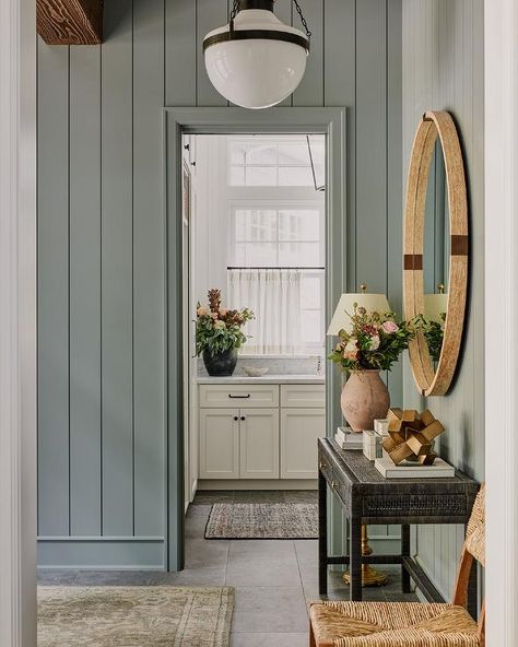 Blue shiplap trim accents a foyer boasting a black cane console table, styled and located under a round brown mirror. Cottage Paint Colors Interior, Mudroom Paint, Lake House Paint Colors, Mudroom Paint Color, Entryway Colors, Entryway Paint Colors, Cottage Paint Colors, Green Grey Paint, Office Paint Colors