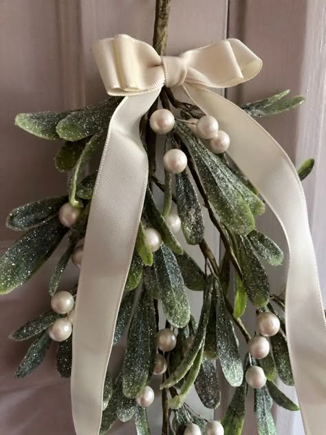 ‘Christmas Kisses’ Traditionally hung above doorways at Christmastime, it’s said that kissing under the mistletoe brings good luck for the year ahead. Handmade from a generous bunch of quality faux mistletoe, dusted with pretty white fine glitter and adorned with pearlised berries. Tied with a fabric bow in your choice of classic ivory or festive red. Complete with integral hook. Average length of 40cms. Kiss Under The Mistletoe Aesthetic, Mistletoe Decoration Christmas, Mistletoe At Wedding, Mistletoe Wedding Decoration, Mistletoe Centerpiece, Mistletoe Doorway, Christmas Mistletoe Aesthetic, Mistletoe Ideas, Mistletoe Aesthetic