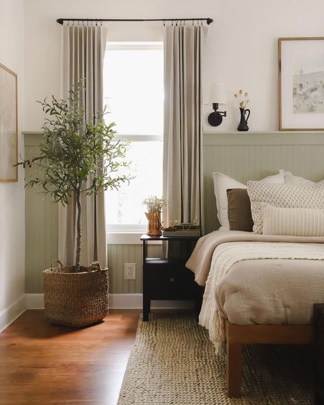 I wish this were my dreamy cottage bedroom. The color palatte is so beautiful, and all the natural materials in the room make it feel so grounded. The most impactful part of this room is the accent wall with the pale sage green wainscoting. This adds some color and life to the room and acts as a headboard substitute for the bed and a hidden shelf for extra dÃ©cor items. Cottage Bedroom Wainscoting, Sage Green Headboard Bedroom, Light Sage Accent Wall, Sage Green Wainscoting Bedroom, Gray Green Wainscotting, Cream Sage Bedroom, Pale Green Furniture, Sage Green Natural Bedroom, Bedroom Light Green Accent Wall