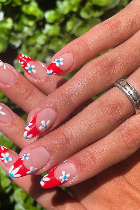 The almond-shaped nails showcase a playful twist on a floral theme with a vivid red backdrop. Each nail features charming white daisies accented by small blue dots at the center, giving a fresh and cheerful vibe perfect for any spring or summer occasion.  // Photo Credit: Instagram @jazzed.nailz Summer Fourth Of July Nails, July Nail Inspiration, Red July Nails, 4th Of July Nails Flowers, Almond Red White And Blue Nails, Cute Nails Summer Almond, 4th Of July Inspired Nails, 4th Of July Nail Designs Blooming Gel, Red Nails 4th Of July