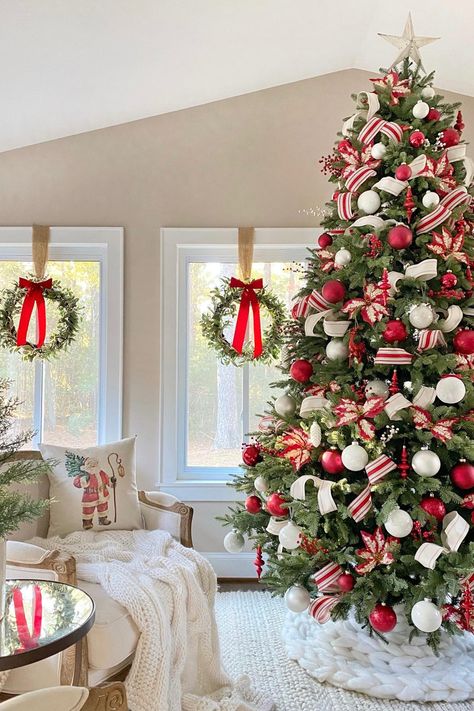 A Christmas tree decorated with red and white ornaments and ribbon, in front of windows with wreaths hanging in them with red bows. Candy Cane Home Decor, Red Snd White Christmas Tree, Christmas Styles Decor, Christmas Tree Decorations Red And White, White Red Christmas Decor, Red Christmas Decor Ideas, Christmas Tree Red White, Christmas Tree Red And White, Red Christmas Tree Decorations