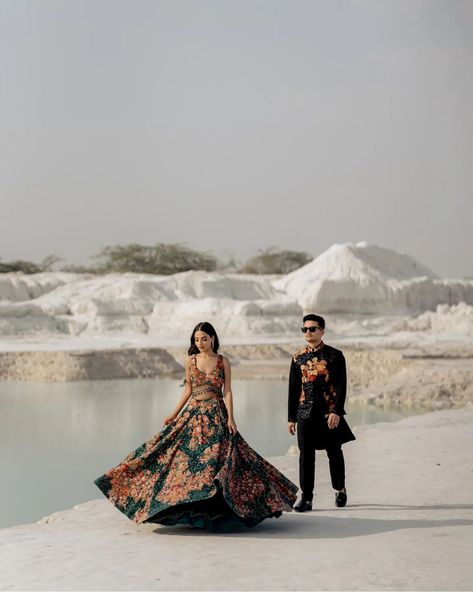 The bride-to-be is dressed in an elegant, flowy lehenga with vibrant floral prints, which brings a sense of movement and grace to the image. Her long, wavy hair cascades over her shoulders as she walks, adding a touch of soft femininity to the composition. The groom-to-be complements her look in a black kurta with matching floral accents, exuding a contemporary yet traditional vibe. The composition of the shot feels balanced and artistic, with the groom standing relaxed against the tree whil... Jaipur Prewedding Shoot, Jaipur Pre Wedding Shoot, Jaipur Prewedding, Flowy Lehenga, Prewedding Shoot, Black Kurta, Pre Wedding Poses, Pre Wedding Shoot, Jaisalmer