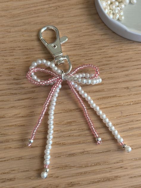 The cutest little accessories for your bags. Shaped in a bow shape, with acrylic pearl beads and pink glass beads. Comes with either gold or silver hardware. Bow Bag Charm, Pearl Key Chain, Diy Beaded Bow, Easy Things To Sell At Craft Fairs, Bead Bag Charm, Bag Charms Beads, Stuff To Make With Beads, Cute Beaded Keychains, Diy With Pearls