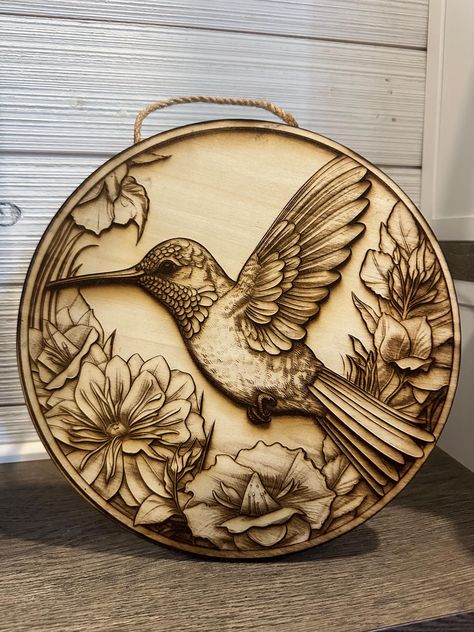 Laser engraved 3D illusion wooden plaque features picturesque humming bird. Plaque is a high quality craft plywood and is sealed using a satin finish clear coat. Plaque is approximately 12" wide Ideal for indoor décor, decoratively placing on a shelf or displaying on a wall using the included jute rope. **Please note: Items are made on different pieces of wood and given the nature of natural materials used, there may be slight differences in wood spots, wood grains, etc. Wood Carving Wall Art, Bird Wall Hanging, Wood Burning Patterns Stencil, Wood Burning Stencils, Hummingbird Wall Art, Wood Art Diy, Wood Burn Designs, Illusion 3d, Woodburning Projects